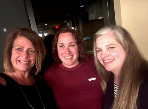 Three smiling women posing together for a photo indoors at what appears to be an event or venue